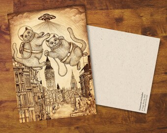 Op de afbeelding: Een sepia-getinte illustratie van twee katten in ruimtepakken die boven een gedetailleerde stadsgezicht zweven, met een UFO boven hen. Het kunstwerk staat op een ansichtkaart, met een blanco kaart ernaast. De tekst "Cosmonauts in London" is zichtbaar.