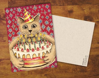 Op de afbeelding: Verjaardagskaart met een illustratie van een kat met een feesthoedje, die een gelaagde taart met brandende kaarsen vasthoudt. De achtergrond is rood met blauwe en gouden sterren. Op een houten oppervlak.