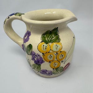 Peut inclure: Une tasse en céramique blanche avec une anse noire et le texte "But First, Coffee" en gras noir. La tasse est posée sur un fond flou, suggérant un cadre chaleureux.