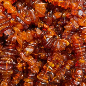 May include: Close-up of a collection of amber gemstone beads. The beads are a warm, translucent orange-brown color, with irregular shapes and sizes. The beads are strung together, creating a textured and organic appearance.