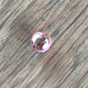 Puede incluir: Una sola piedra preciosa rosa facetada sobre una superficie de madera.