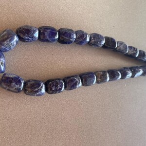 May include: A strand of dark blue, faceted, rectangular gemstone beads. The beads are strung on a clear cord.