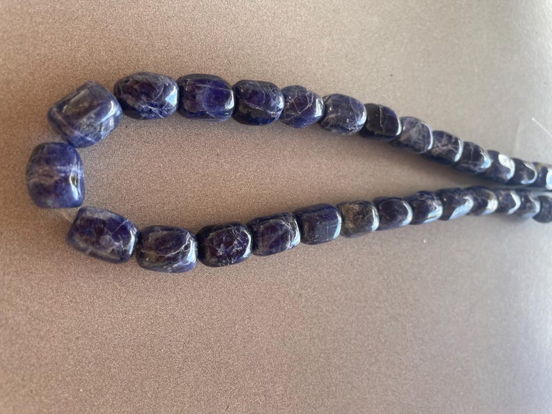 May include: A strand of dark blue, faceted, rectangular gemstone beads. The beads are strung on a clear cord.