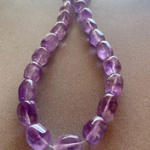 May include: A strand of purple amethyst gemstone beads, each bead is faceted and has a smooth, rounded shape.