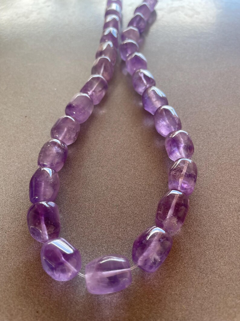 May include: A strand of purple amethyst gemstone beads, each bead is faceted and has a smooth, rounded shape.