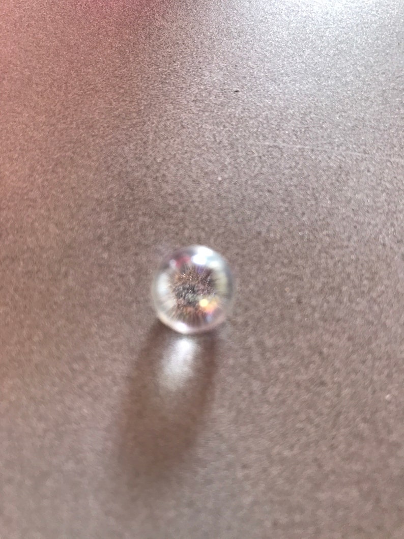 Puede incluir: Una canica de vidrio transparente con un acabado brillante e iridiscente.