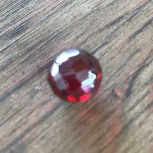 Puede incluir: Una piedra preciosa de color rojo intenso con un corte facetado. La piedra preciosa est&aacute; sobre una superficie de madera.