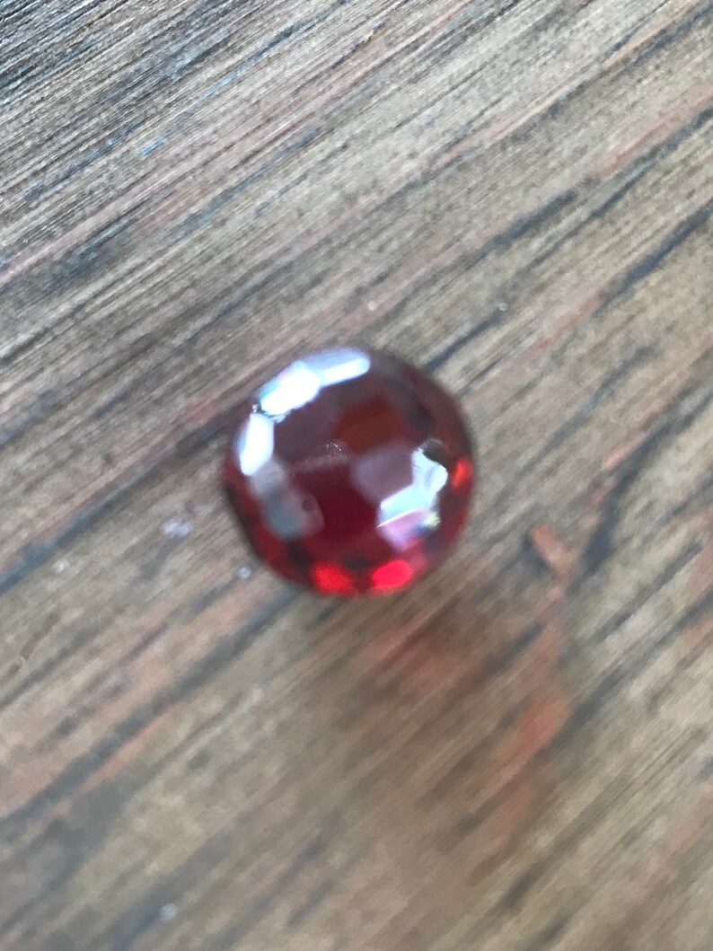 Puede incluir: Una piedra preciosa de color rojo intenso con un corte facetado. La piedra preciosa est&aacute; sobre una superficie de madera.