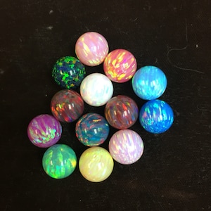 May include: A collection of 13 iridescent opal beads in various colors, including pink, blue, green, and white. The beads are round and smooth, and they are arranged in a loose pile.