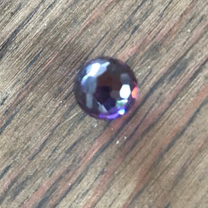 Puede incluir: Una sola gema redonda de color p&uacute;rpura con una superficie facetada.