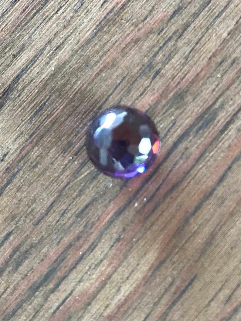 Puede incluir: Una sola gema redonda de color p&uacute;rpura con una superficie facetada.