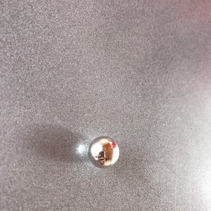 Puede incluir: Un rodamiento de bolas de plata brillante sobre una superficie gris texturizada.