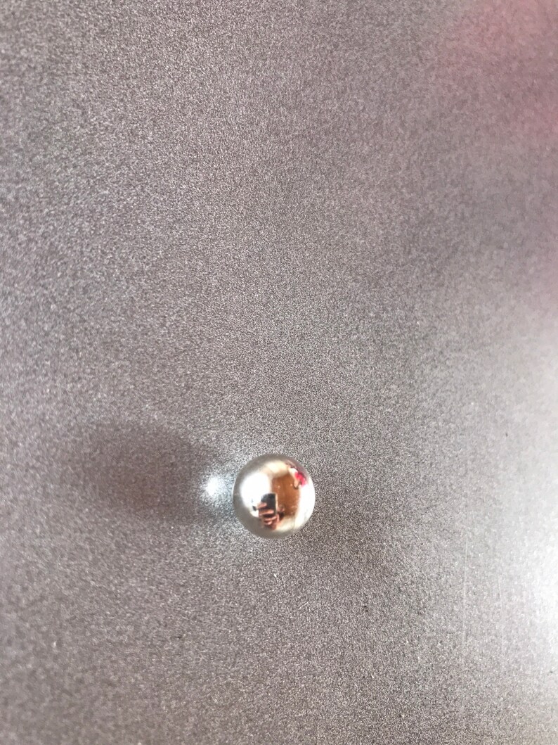 Puede incluir: Un rodamiento de bolas de plata brillante sobre una superficie gris texturizada.