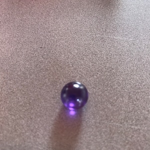 Puede incluir: Un solo m&aacute;rmol de vidrio morado sobre una superficie gris texturizada.