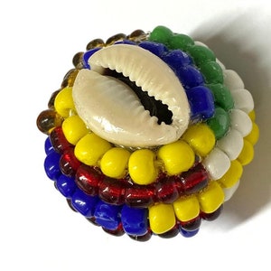 May include: A round bead made of colorful glass beads and a white cowrie shell. The bead is multi-colored with red, yellow, blue, green, and white beads.
