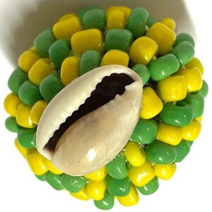 May include: A cowrie shell is surrounded by green and yellow beads, creating a spherical shape.