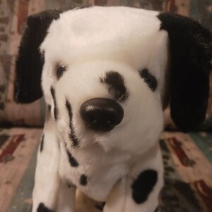 以下が含まれることがあります： 白い毛並みに黒い斑点がある犬のぬいぐるみ。このぬいぐるみは、長く柔らかい黒い耳、滑らかな黒いプラスチック製の鼻、そして暗い色の目を特徴としています。ダルメシアン犬を模したリアルな色合いのデザインになっています。