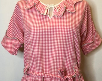 May include: A pink and white gingham dress with a ruffled collar, short sleeves, and a tie belt. The dress has pockets on the sides and a scalloped trim.
