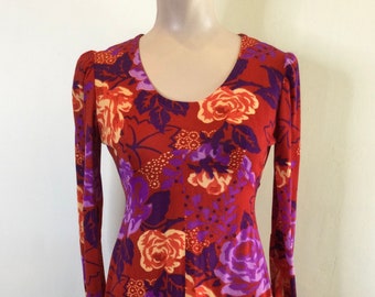 May include: A long-sleeved maxi dress with a red background and a floral print featuring purple, orange, and white flowers. The dress has a scoop neck and long sleeves with a slight puff at the shoulder.