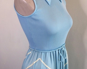 May include: A light blue sleeveless maxi dress with a white trim around the collar and a white braided trim around the hem. The dress has a tie at the waist.