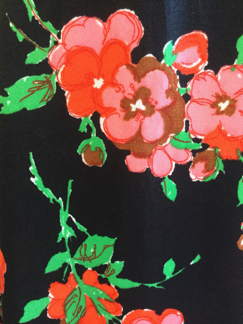 May include: Black fabric with a floral pattern featuring pink, red, and green flowers. The flowers are stylized and have a retro look.