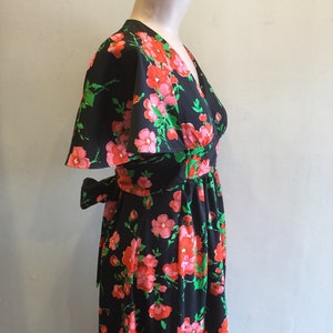 May include: A black maxi dress with a floral print featuring pink and red flowers on a black background. The dress has a V-neckline, short sleeves, and a tie at the waist.