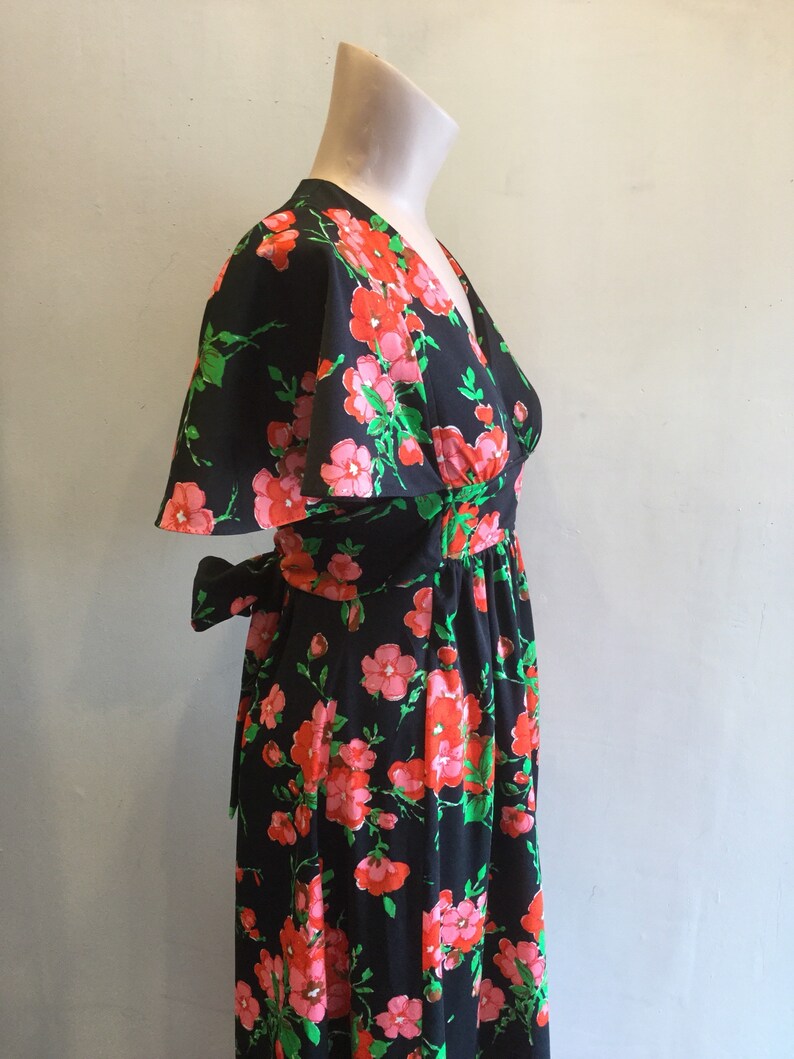 May include: A black maxi dress with a floral print featuring pink and red flowers on a black background. The dress has a V-neckline, short sleeves, and a tie at the waist.