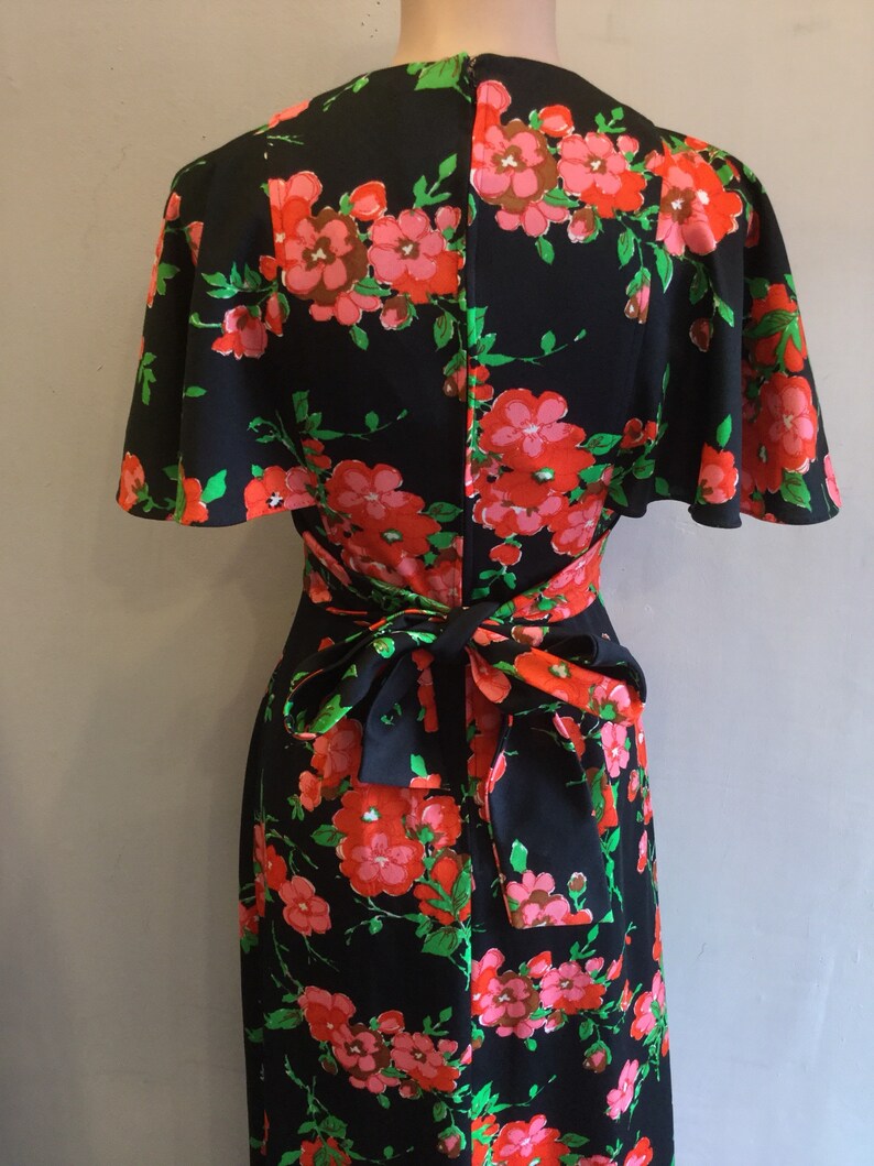 May include: A black maxi dress with a floral print in shades of pink, red, and green. The dress has a wrap style bodice and a tie at the waist.