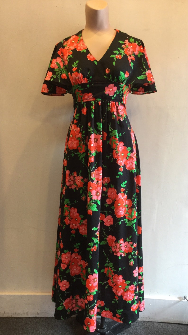 May include: A long black maxi dress with a floral print featuring pink and green flowers. The dress has a v-neckline and short sleeves.