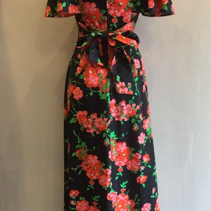 May include: A black maxi dress with a floral print featuring pink and red flowers on a black background. The dress has a V-neckline, short sleeves, and a tie at the waist.