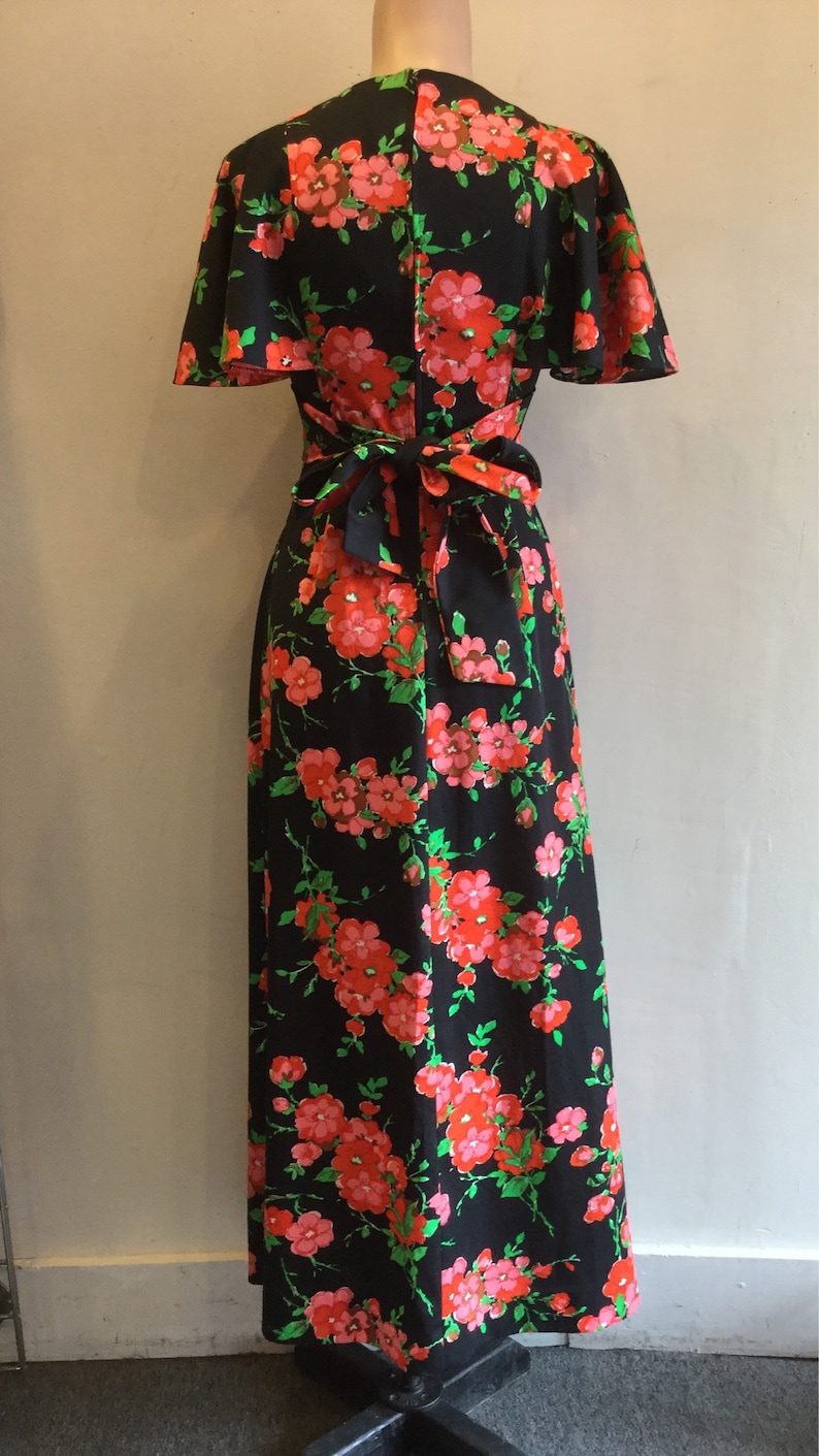 May include: A black maxi dress with a floral print featuring pink and red flowers on a black background. The dress has a V-neckline, short sleeves, and a tie at the waist.