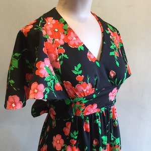 May include: A black maxi dress with a floral print featuring pink and red flowers on a black background. The dress has a V-neckline, short sleeves, and a tie at the waist.