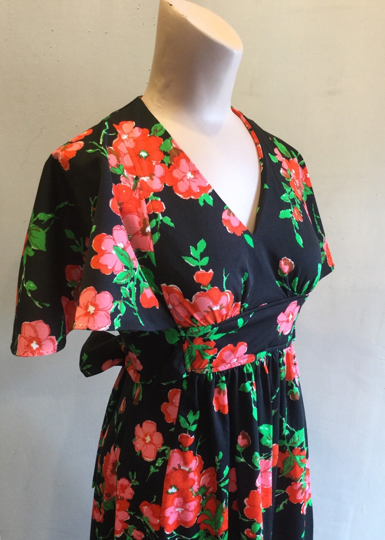 May include: A black maxi dress with a floral print featuring pink and red flowers on a black background. The dress has a V-neckline, short sleeves, and a tie at the waist.