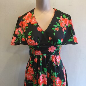 May include: A black maxi dress with a floral print featuring pink and red flowers on a black background. The dress has a V-neckline and short sleeves.