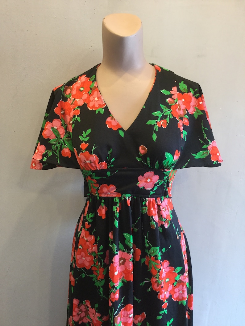 May include: A black maxi dress with a floral print featuring pink and red flowers on a black background. The dress has a V-neckline and short sleeves.