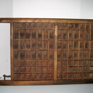 May include: A vintage wooden printing tray with a grid of compartments. The tray is made of dark brown wood and has a worn, rustic appearance.