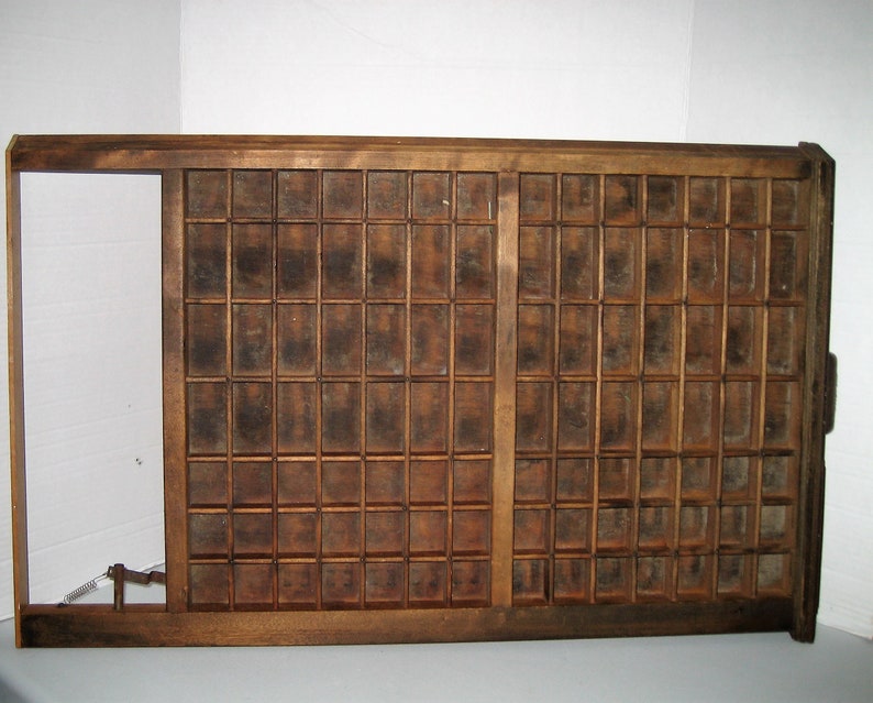 May include: A vintage wooden printing tray with a grid of compartments. The tray is made of dark brown wood and has a worn, rustic appearance.