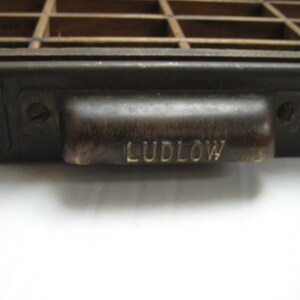May include: A black metal drawer with a brass handle. The handle has the word "LUDLOW" engraved on it.