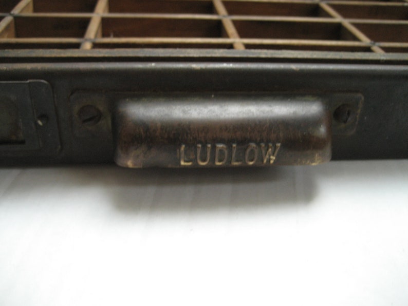 May include: A black metal drawer with a brass handle. The handle has the word "LUDLOW" engraved on it.
