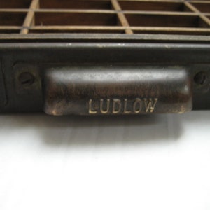 May include: A black metal drawer with a brass handle. The handle has the word "LUDLOW" engraved on it.