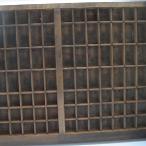 May include: A vintage wooden printing tray with a grid of compartments. The tray is made of dark wood and has a worn, rustic appearance.