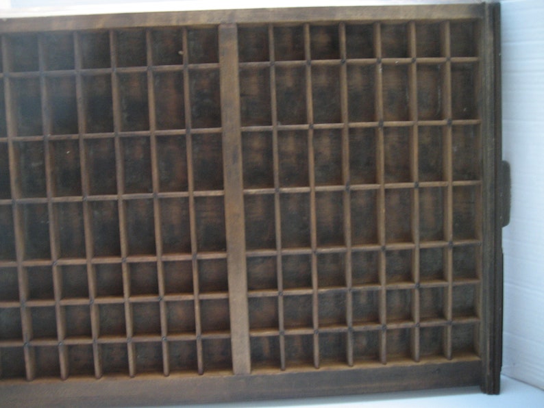 May include: A vintage wooden printing tray with a grid of compartments. The tray is made of dark wood and has a worn, rustic appearance.