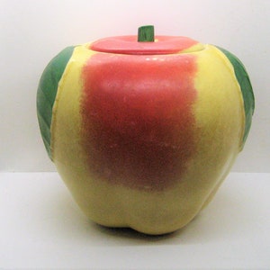May include: A ceramic apple-shaped cookie jar with a lid. The jar is yellow, red, and green. The lid is red and has a green stem.