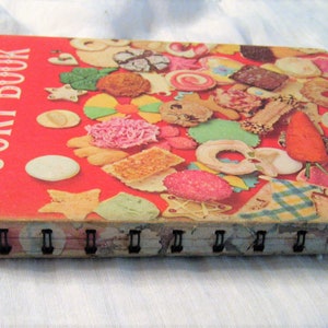 May include: Vintage "Betty Crocker's Cooky Book" with a red cover and spiral binding. The cover features a collage of colorful cookies and the title in white. The book's edges show wear, indicating its age.