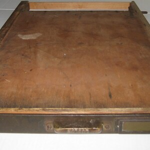 May include: A wooden drawer with a dark brown finish and a brass handle. The drawer is open and the inside is empty.