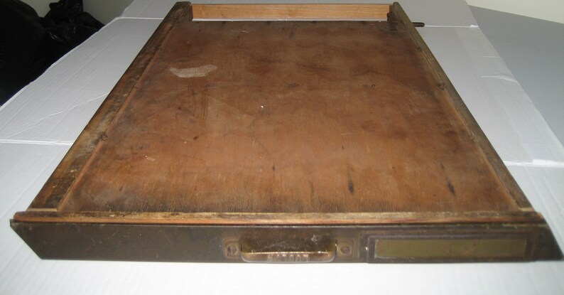 May include: A wooden drawer with a dark brown finish and a brass handle. The drawer is open and the inside is empty.