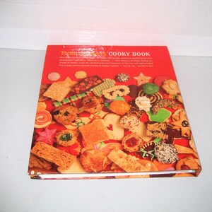 May include: A cookbook titled "Betty Crocker's Cooky Book" with a red cover. The cover features a collage of various cookies, including stars, squares, and round shapes. The book's title is in white letters.