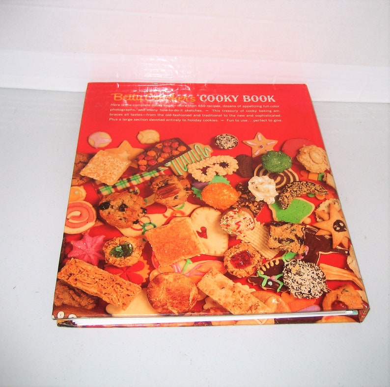 May include: A cookbook titled "Betty Crocker's Cooky Book" with a red cover. The cover features a collage of various cookies, including stars, squares, and round shapes. The book's title is in white letters.