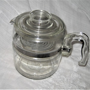May include: A clear glass percolator coffee pot with a glass lid and a glass handle. The pot has a metal band around the middle.