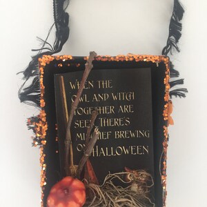 Pu&ograve; includere: Una scatola decorativa a tema Halloween con manico nero e bordo glitterato arancione. All'interno, una carta nera con testo dorato recita: "Quando il gufo e la strega si vedono insieme, c'&egrave; malizia in preparazione ad Halloween".